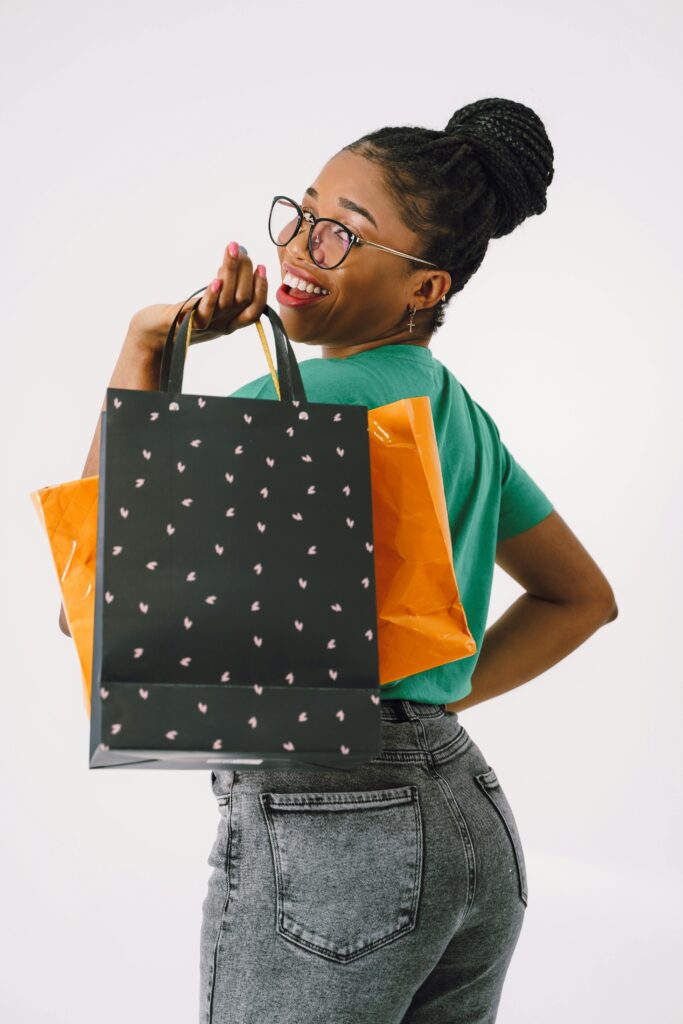 Smiling woman in glasses holding shopping bags against a white background.